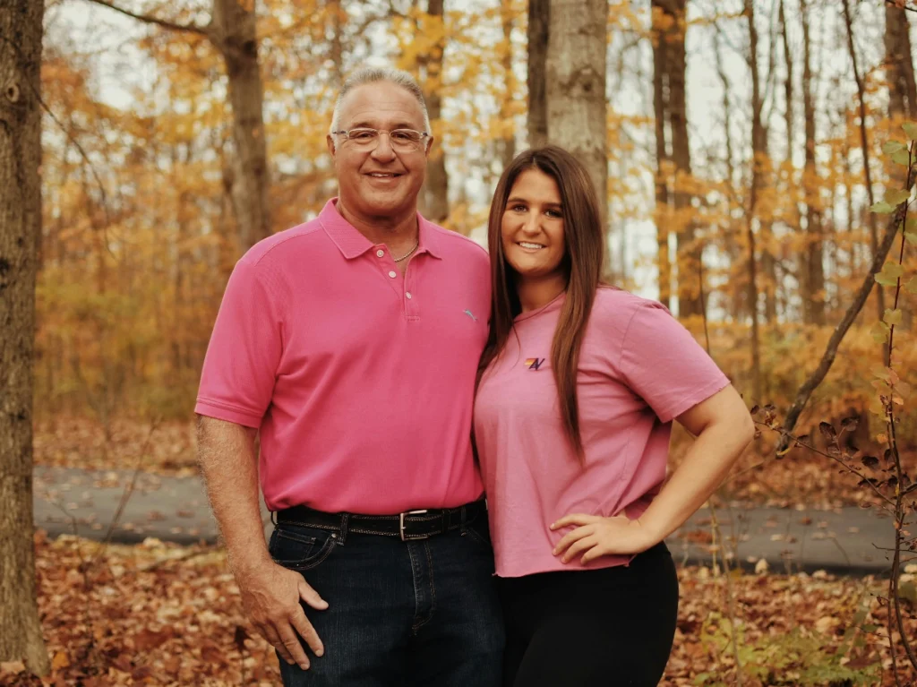 Padre e hija posando juntos felices en un bosque durante el otoño con ropa color rosa.