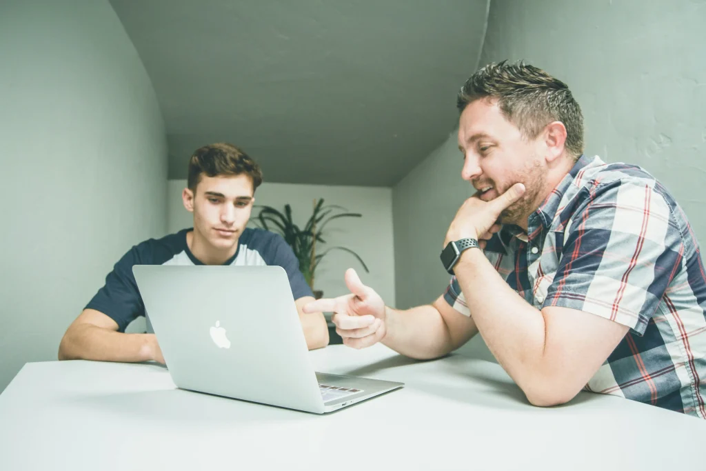 Padre enseñando a su hijo adolescente frente a una laptop, fomentando la educación tecnológica familiar.