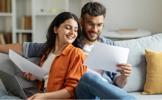 Pareja joven revisando documentos en casa, planeando su futuro financiero con un seguro de vida confiable.