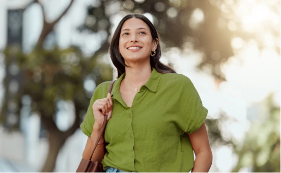 Mujer joven camina sonriente con seguridad, disfrutando del sol, representando confianza y bienestar personal asegurado.