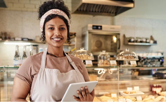 Trabajadora de panadería sonriente con tablet, representa seguridad laboral y protección mediante seguro de vida.