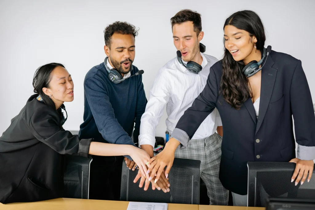 Grupo de jóvenes profesionales uniendo sus manos en señal de trabajo en equipo dentro de oficina moderna.