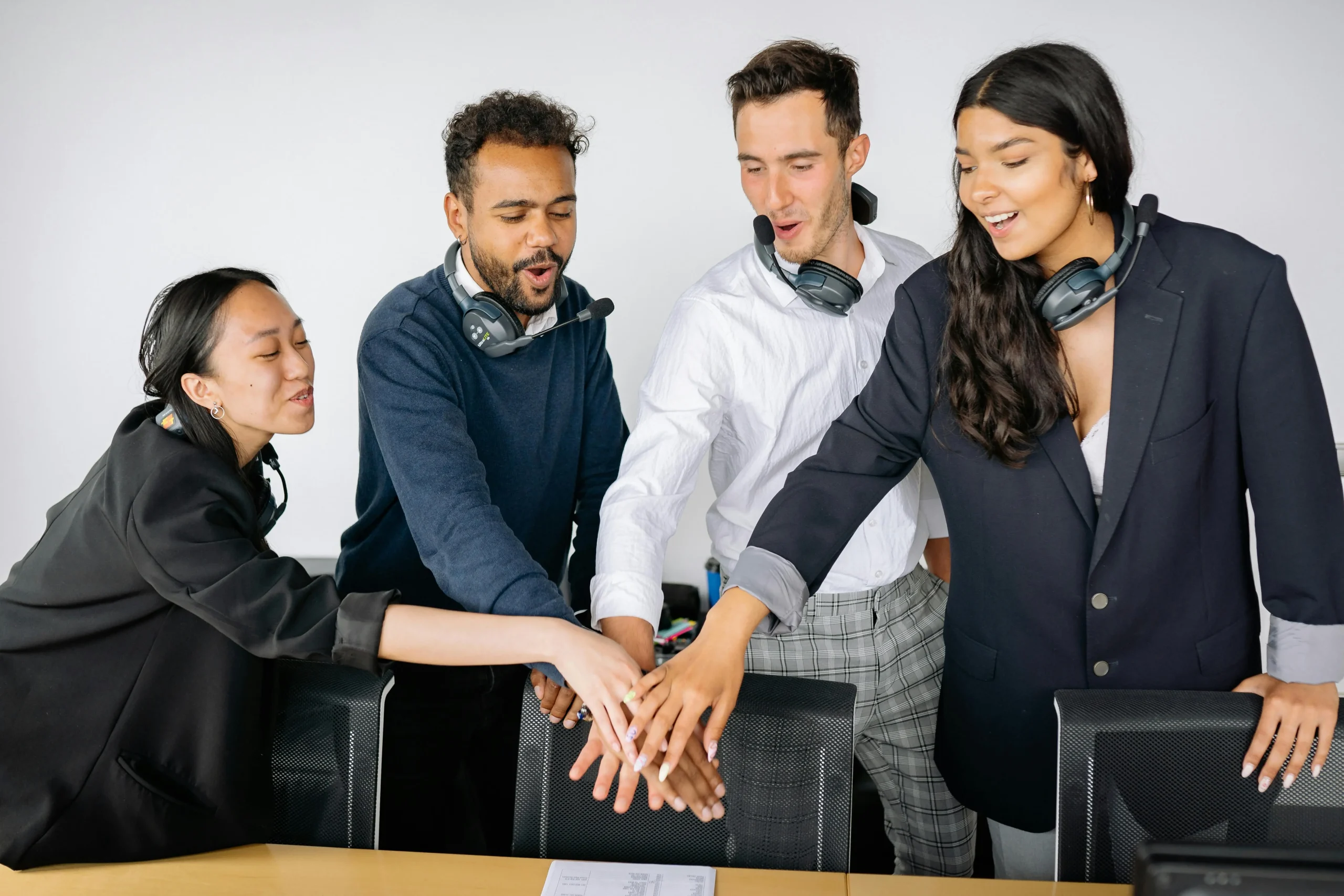 Grupo de jóvenes profesionales uniendo sus manos en señal de trabajo en equipo dentro de oficina moderna.